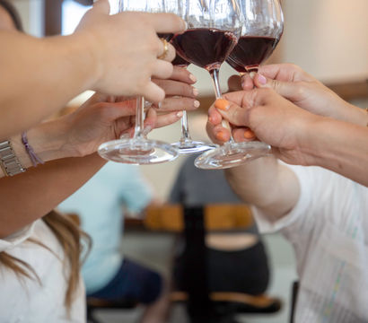 Group cheers with red wine glasses clinking above a 'Reserved' sign on a restaurant table — casual wine-tasting vibe.