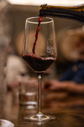 Close-up of deep red wine being poured from a bottle into a tall stemmed glass on a dimly lit restaurant table, cozy wine bar ambiance