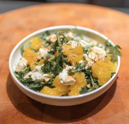 Citrus arugula salad with bright orange segments, crumbled goat cheese and chopped nuts in a white bowl on a wooden cutting board