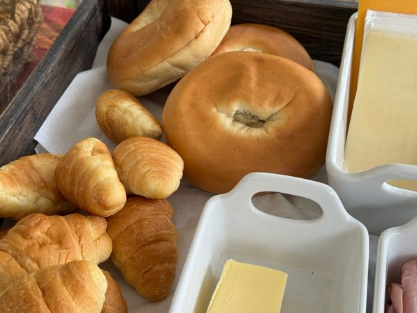 Golden mini croissants and round bagels on a wooden breakfast tray with butter and sliced cheese, continental breakfast spread