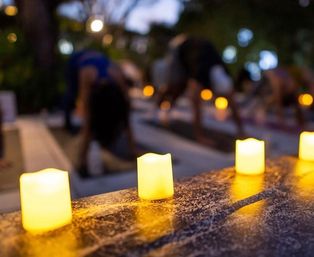 Glowing LED tea lights on a stone ledge with a blurred outdoor twilight yoga class in the background