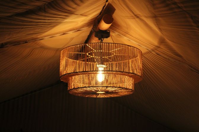 Warm amber glow from a double-tier woven rattan chandelier with exposed bulb, hanging from a fabric tent ceiling
