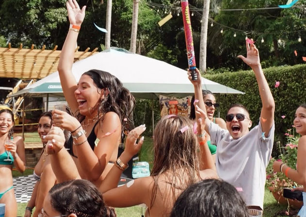Sunny backyard pool party with young adults cheering, throwing confetti under palm trees