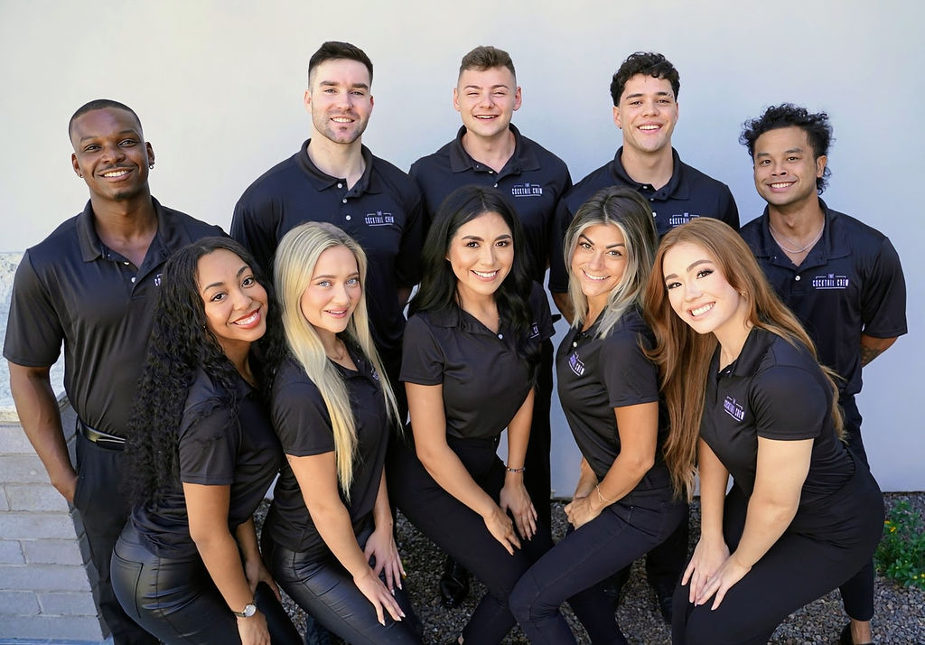 Smiling group of young professionals in matching black polo shirts posing outdoors against a light wall — upbeat team photo for staff, corporate team, and business profile.