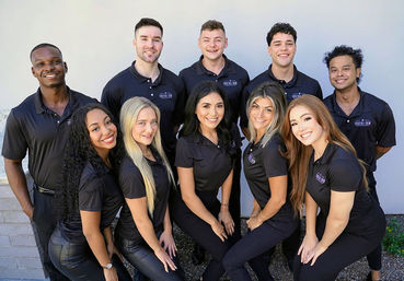 Smiling, energetic team of ten young professionals in matching black polo shirts posing outdoors against a light wall — group staff photo for a service business.