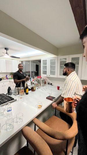 Friends chatting at a modern white home kitchen island turned casual bar, with liquor bottles, glassware, bar stools and a copper mug.