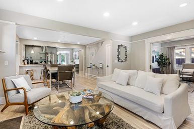 Bright, airy open-concept living room and kitchen with white sofa, wood-and-glass coffee table, dining area and light hardwood floors — modern neutral decor.