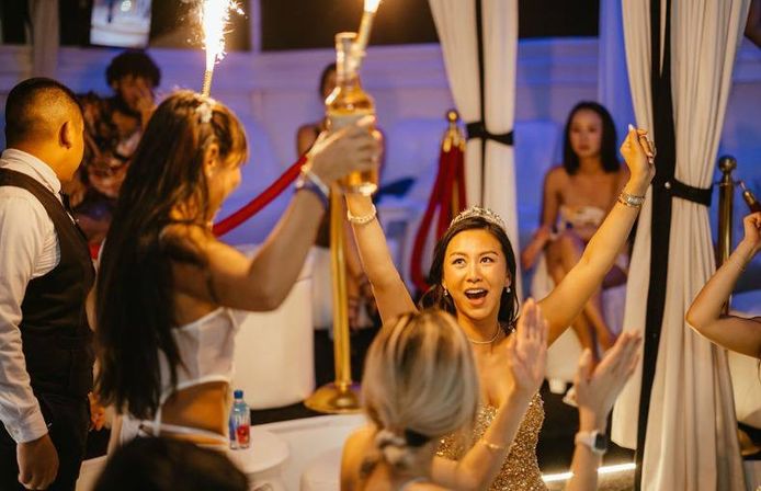 Woman wearing a tiara cheering at a VIP nightclub table as friends present bottle service with sparklers during a celebratory night out