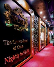 Glamorous nightclub entrance with ornate gold signage, decorative geometric wall panels and a red carpeted walkway lit by recessed ceiling lights, hinting at late-night, resort-style nightlife.