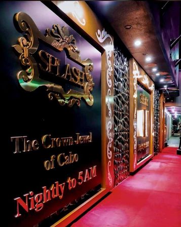 Glamorous nightclub entrance with ornate gold signage, decorative geometric wall panels and a red carpeted walkway lit by recessed ceiling lights, hinting at late-night, resort-style nightlife.
