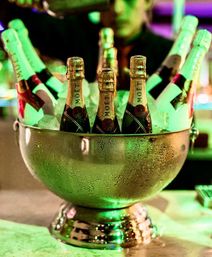 Silver ice bucket filled with chilled champagne bottles glowing under green bar lighting