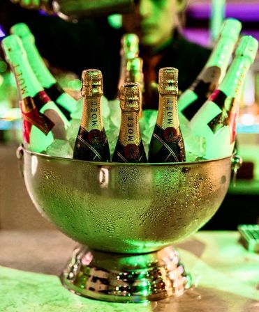 Silver ice bucket filled with chilled champagne bottles glowing under green bar lighting