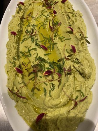 Creamy green hummus drizzled with olive oil, topped with chopped herbs and red microgreens, served on a white oval platter — Mediterranean-style appetizer.