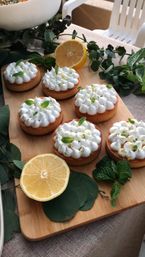 Zesty mini lemon meringue tarts on a wooden board, topped with piped meringue, fresh mint leaves, lemon halves and eucalyptus garnish