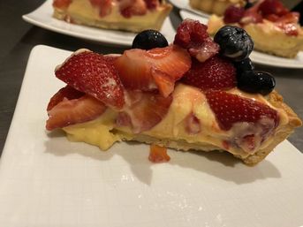 Close-up of a slice of strawberry and blueberry fruit tart — flaky pastry filled with creamy vanilla custard and glazed fresh berries on a white plate.