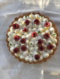 Top-down view of a lemon tart with piped white meringue peaks, fresh raspberries, lemon zest curls and mint leaves in a golden scalloped pastry crust on a light linen cloth