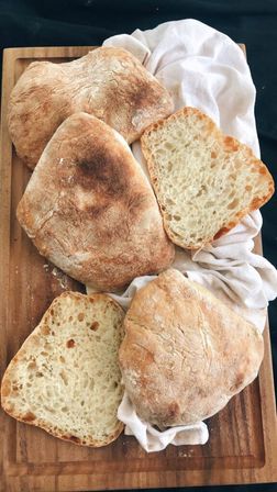 Fresh rustic ciabatta loaves and open halves showing airy crumb on a wooden cutting board with a white linen cloth