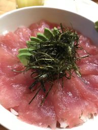 Close-up of Japanese tuna sashimi donburi: thin pink tuna slices fanned over white sushi rice, topped with shredded nori and avocado slices