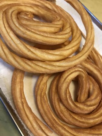 Close-up of golden spiral churros with ridged texture on a parchment-lined tray — crispy fried pastry dessert.