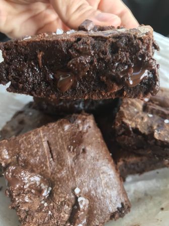 Close-up of fudgy chocolate chip brownies with gooey melted chocolate and flaky sea salt, hand holding a square