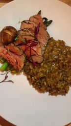 Sliced pink roast beef with grilled asparagus, a roasted baby potato, microgreens and savory brown risotto artfully plated on a white dinner plate — gourmet restaurant-style entrée