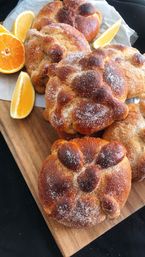 Golden pan de muerto rolls dusted with sugar on a wooden board, served with fresh orange wedges and parchment paper — Mexican sweet bread pastry