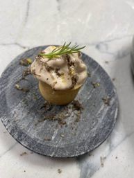 Mini savory tartlet topped with creamy mousse, shaved truffle and a microgreen sprig on a round slate serving plate set on white marble countertop
