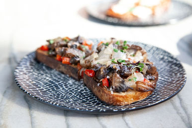Savory mushroom and roasted red pepper toast on crusty sourdough with melted cheese, caramelized onions and microgreens served on a patterned black plate — gourmet brunch dish