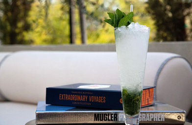 Refreshing tall crushed-ice mint cocktail with a sprig of mint and straw, set beside stacked coffee-table books on an outdoor patio lounge table