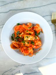 Overhead shot of shrimp pasta in creamy tomato sauce topped with chopped basil, served in a white bowl on a marble tabletop with a gold fork.
