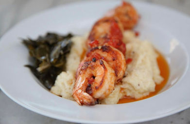 Plump seared shrimp lined atop creamy grits with braised collard greens and a buttery orange sauce on a white plate — Southern-style shrimp and grits.