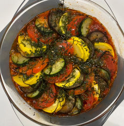 Vibrant ratatouille-style baked vegetables in a round glass dish — layered zucchini, yellow squash, eggplant and tomato slices in herbed tomato sauce.