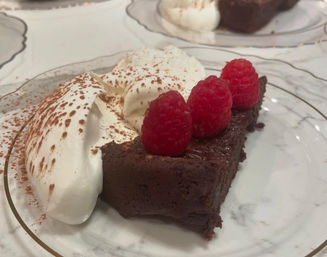 Decadent chocolate tart slice topped with three fresh raspberries, served with cocoa-dusted whipped cream on a decorative dessert plate.