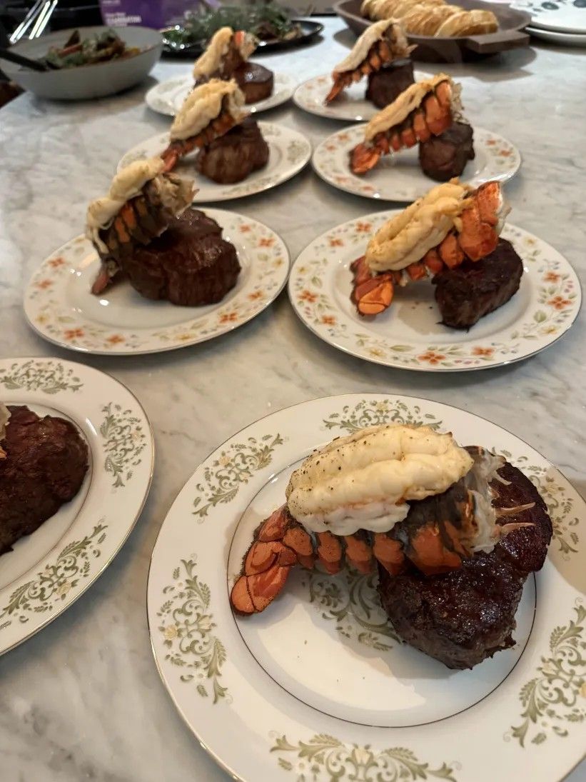 Elegant surf-and-turf plates with lobster tails perched on filet mignon, served on vintage floral china atop a marble countertop
