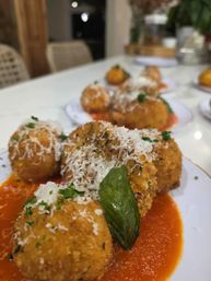 Close-up of golden fried arancini (risotto balls) on white plates over marinara sauce, sprinkled with grated Parmesan and parsley and garnished with a basil leaf — Italian appetizer in a modern dining setting.