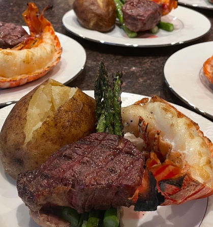 Gourmet surf-and-turf plate: seared filet mignon, grilled lobster tail, baked potato and roasted asparagus on a white plate