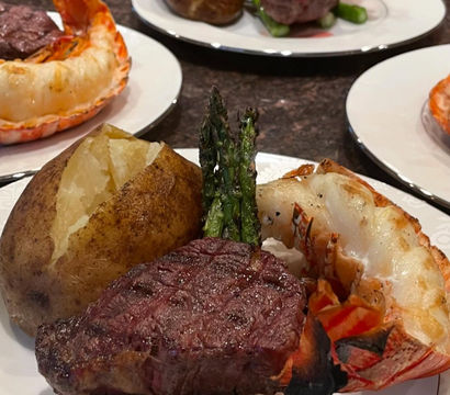 Gourmet surf-and-turf plate: seared filet mignon, grilled lobster tail, baked potato and roasted asparagus on a white plate