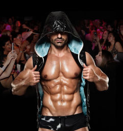 Muscular male dancer in a hooded vest and shiny black shorts showing an oiled six-pack on a nightclub stage while excited women in the crowd cheer and take photos