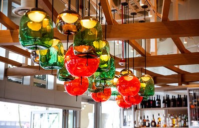 Vibrant red and green blown-glass pendant lights clustered beneath wooden beams in a modern restaurant bar interior, with liquor bottles on back shelves.