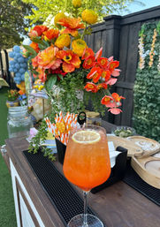 Zesty orange cocktail with lemon slice on a wooden outdoor bar, vibrant orange-yellow flower centerpiece and festive backyard party decor
