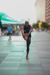 Barefoot athlete balancing on one leg and holding his outstretched foot on a tiled city plaza — outdoor urban yoga/fitness scene