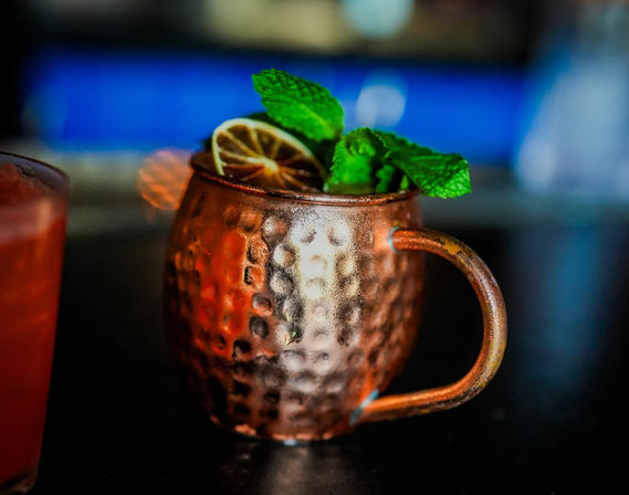 Icy hammered copper Moscow Mule mug topped with a lime wheel and vibrant mint sprig on a dim bar counter with colorful bokeh lights