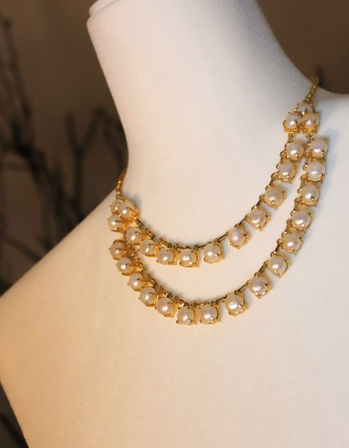 Layered gold-tone pearl necklace with creamy round pearls in floral prong settings, draped on a white display bust.