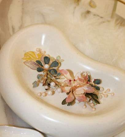 Delicate pastel floral bridal hairpins with pink and teal enamel petals, gold wire and pearl accents resting in a cream ceramic dish