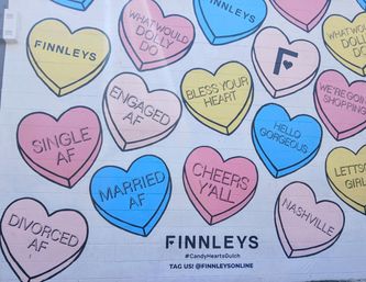 Colorful Nashville mural of oversized pastel candy hearts on a brick wall, each heart displaying playful phrases like Single AF, Married AF, Bless Your Heart and Cheers Y'all.