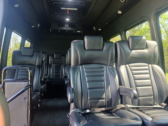 Spacious luxury passenger van interior with plush black leather captain seats, armrests, overhead emergency hatch and large windows showing green trees outside