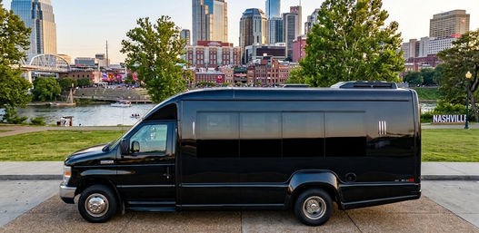 Black passenger shuttle parked on the Nashville riverfront with the river and downtown skyline at sunset.