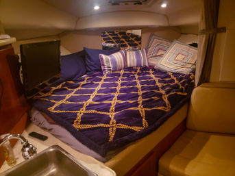 Cozy yacht cabin berth with navy blanket patterned like yellow rope, striped and geometric pillows, small TV and compact sink area
