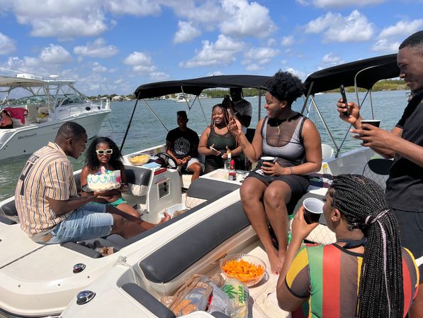 Friends celebrating a birthday on a motorboat in sunny coastal waters, sharing cake, drinks and snacks near other boats