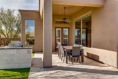 Sunlit Southwestern-style stucco patio with a wicker outdoor dining set, ceiling fan, built-in stainless grill and desert landscaping